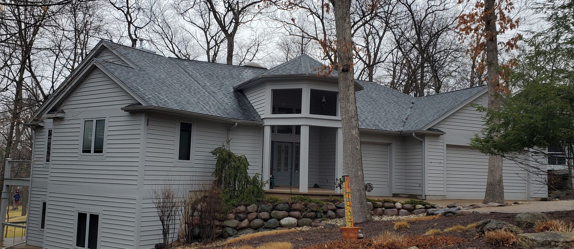 A large white house with a gray roof is surrounded by trees.