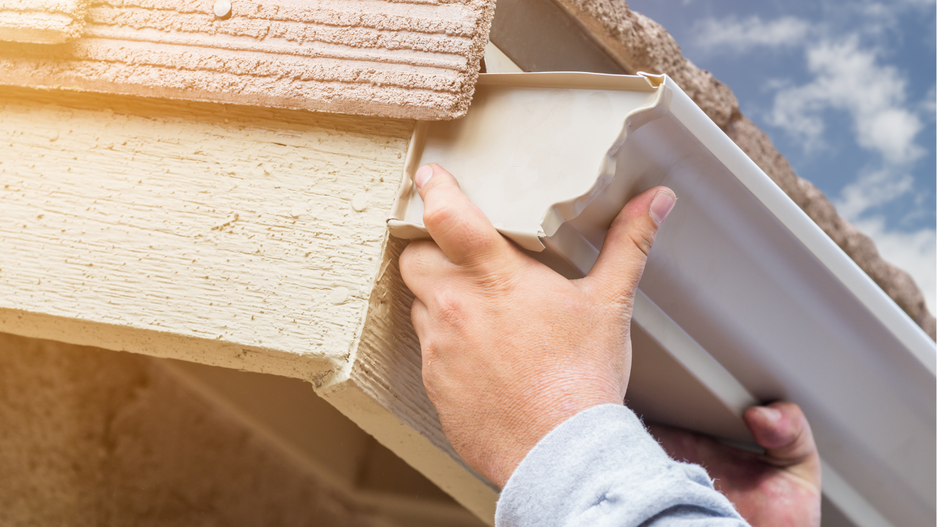 A man is installing a gutter on the side of a house.