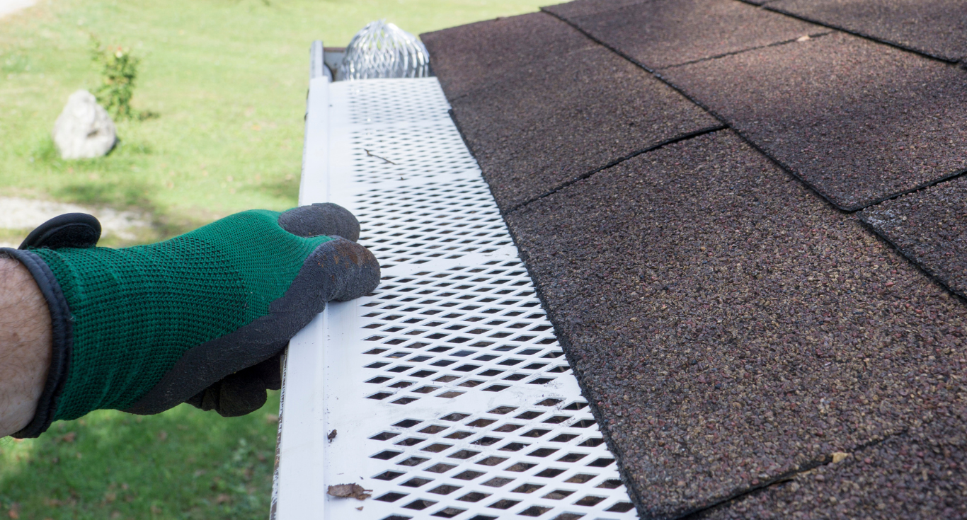 A person wearing gloves is cleaning a gutter on a roof.