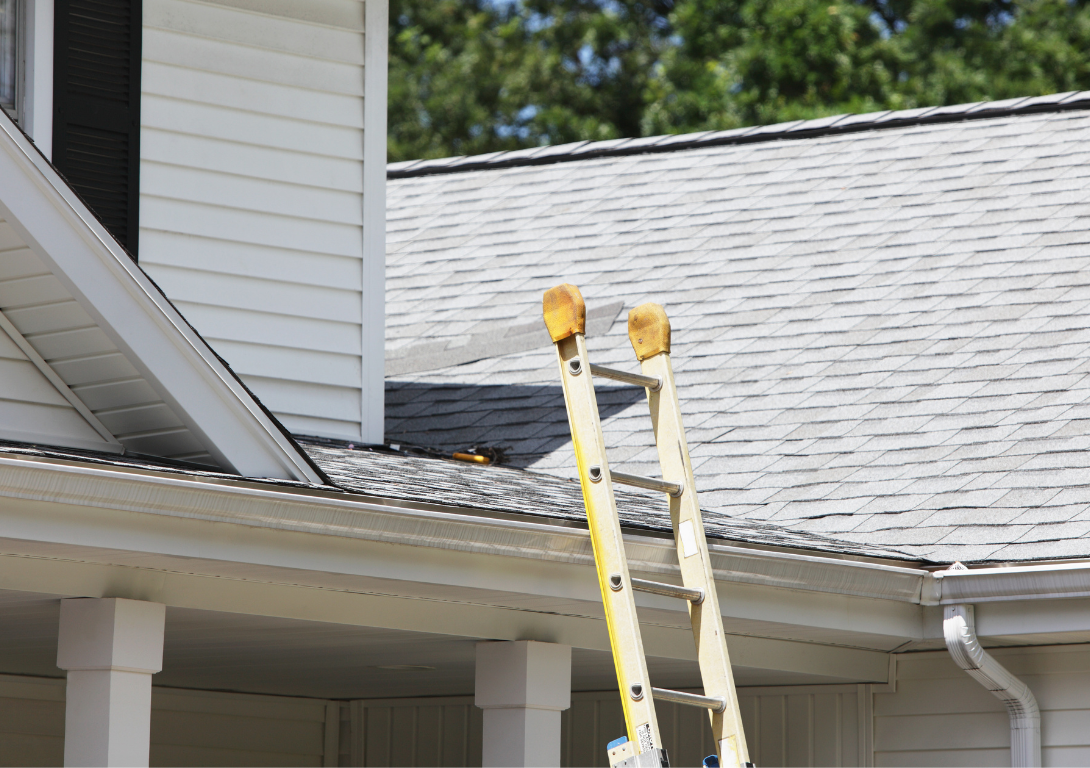 A person is standing on a ladder on the roof of a house.