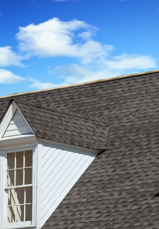 The roof of a house with a window and a blue sky in the background.