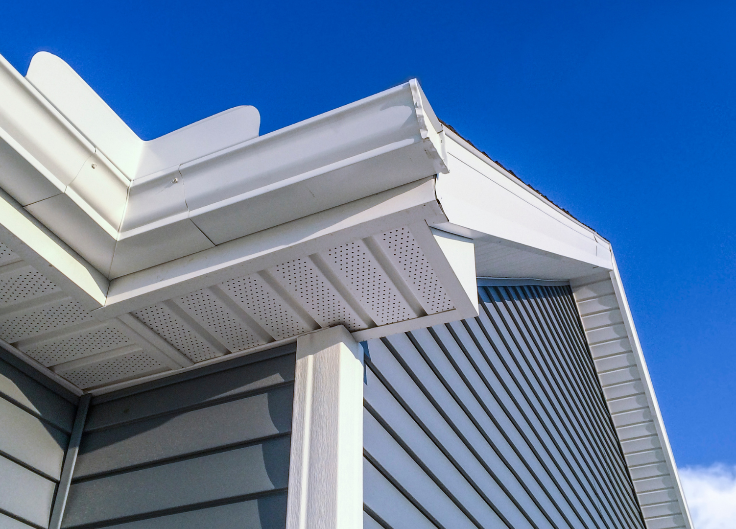 The roof of a house with a white gutter and a blue sky in the background.