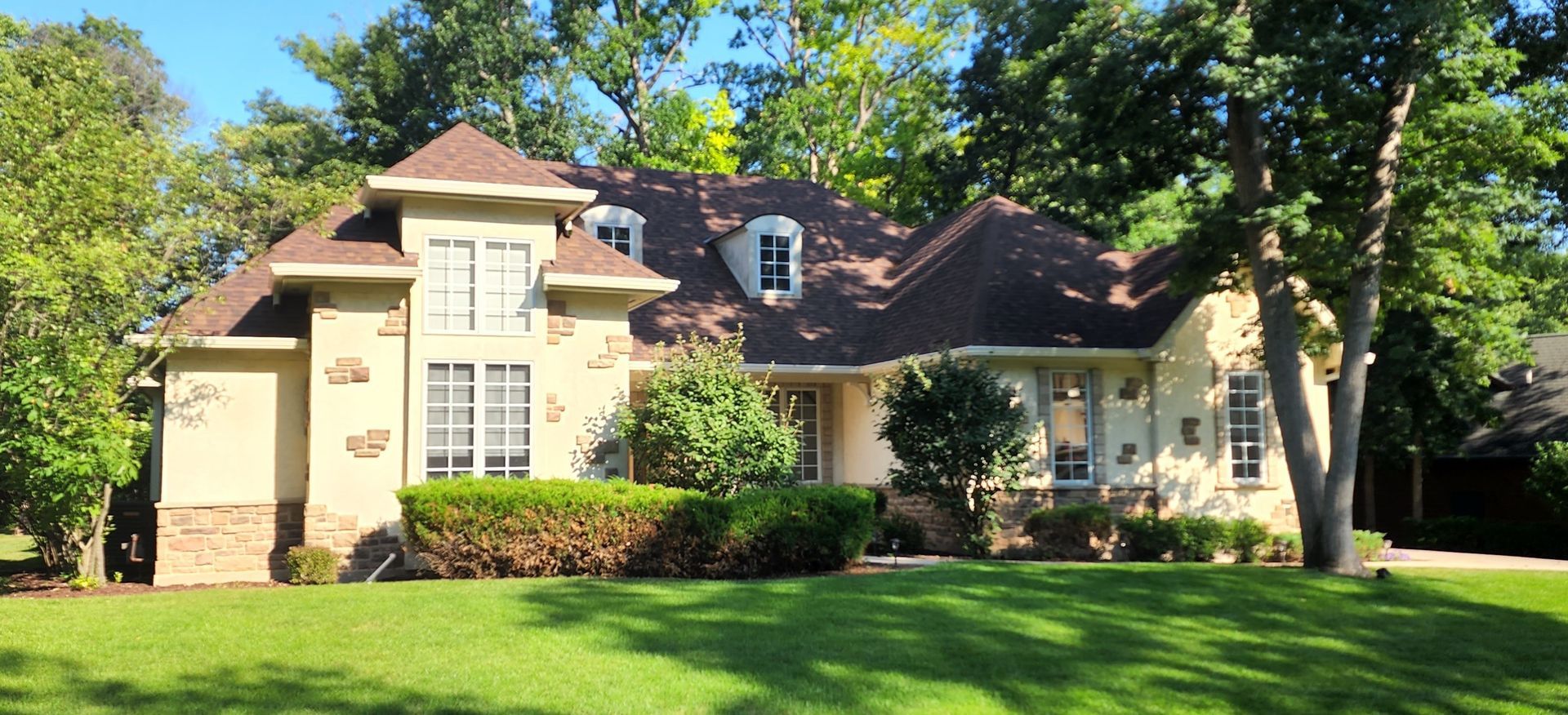 A large house with a brown roof is sitting on top of a lush green lawn.