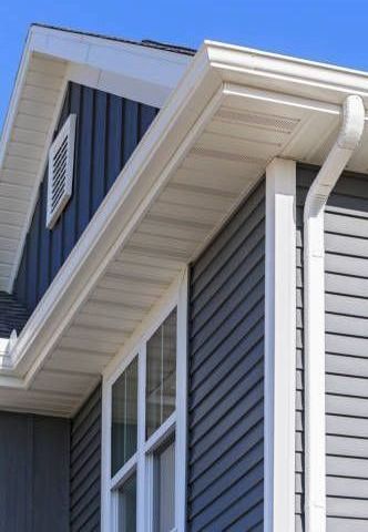 A gray house with a white gutter and a blue sky in the background.