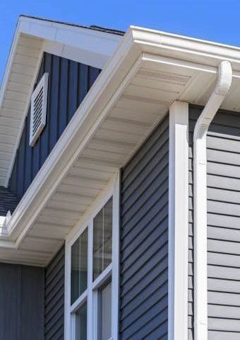 A gray house with a white gutter and a blue sky in the background.
