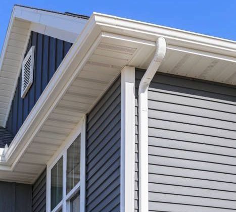 A gray house with a white gutter and a blue sky in the background.