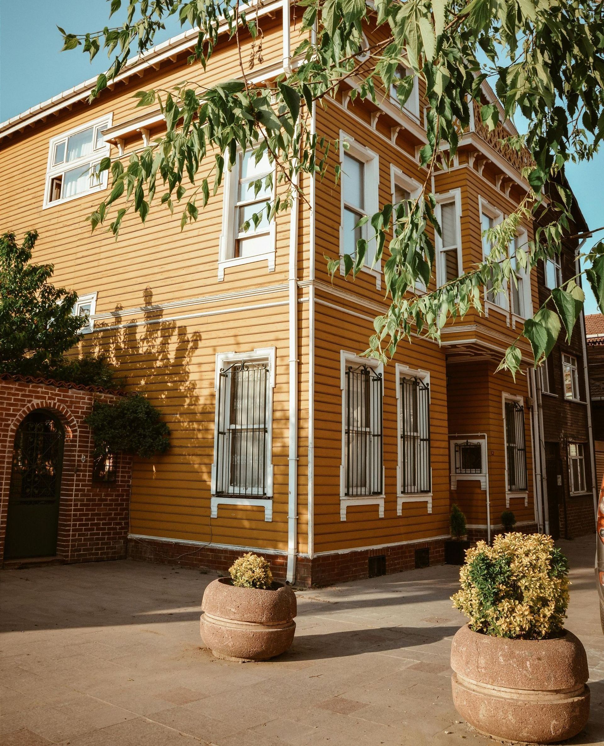 A large yellow house with a lot of windows and potted plants in front of it.