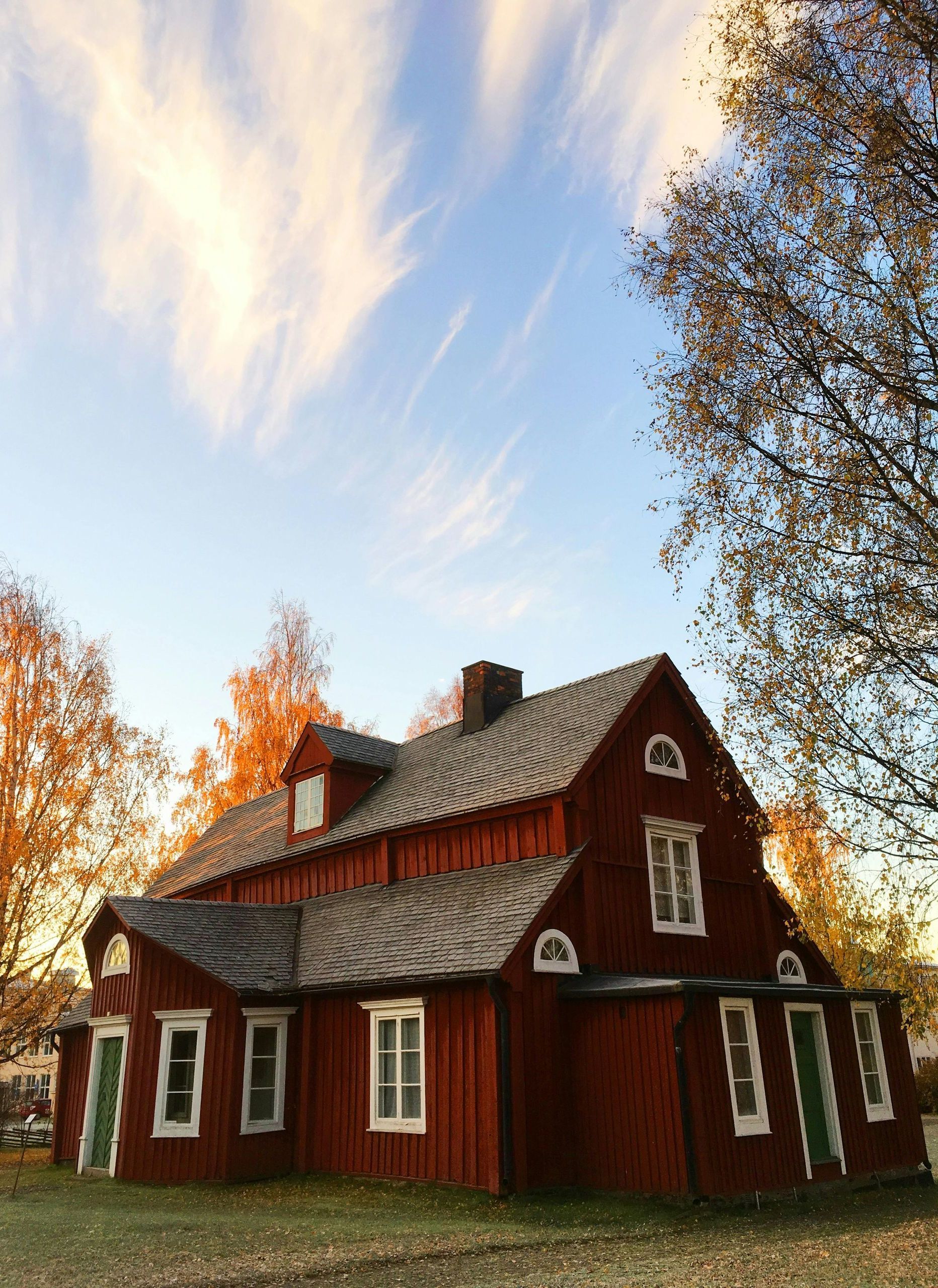 A red house with a slate roof is surrounded by trees and a blue sky.