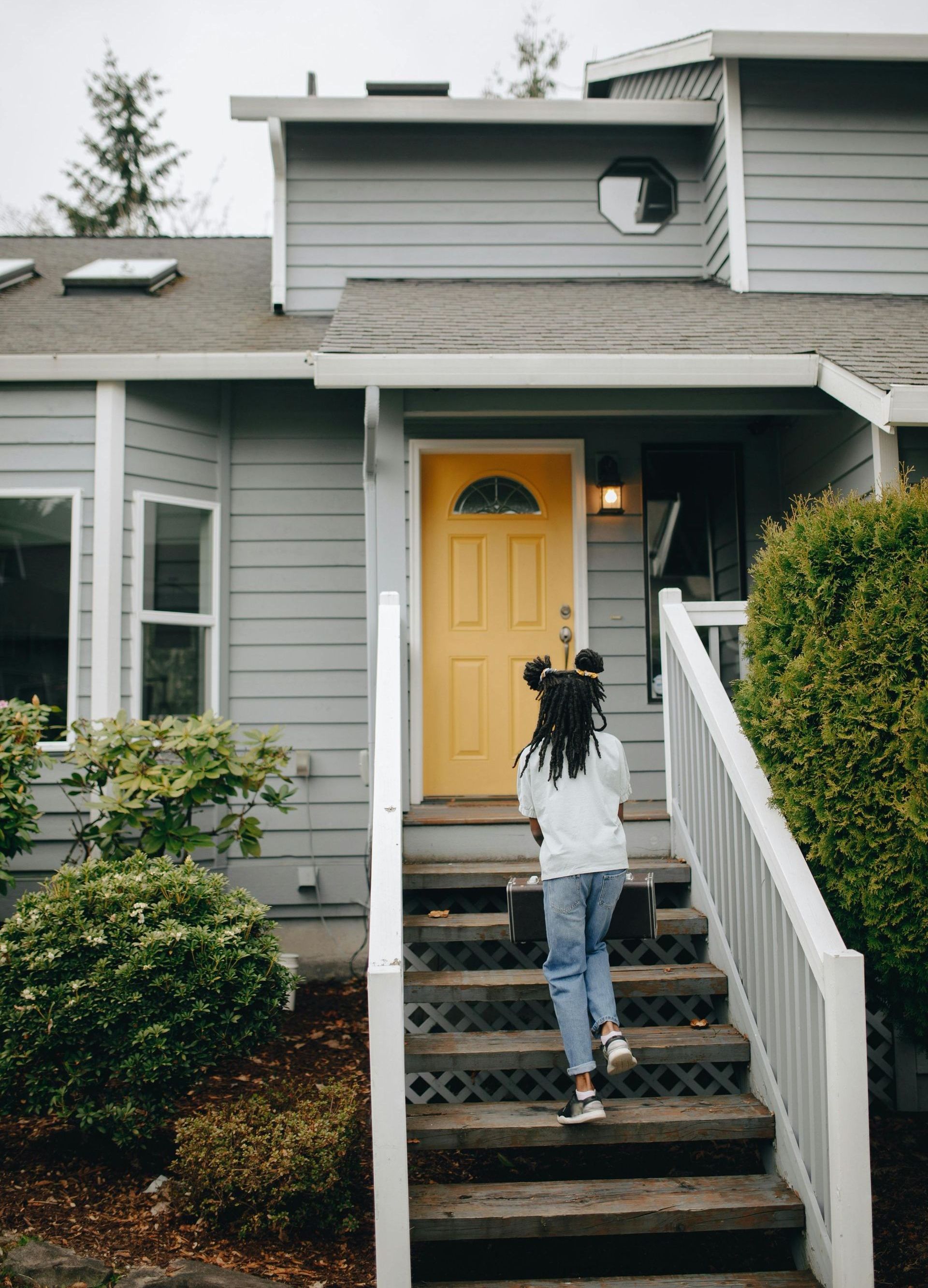 A girl is walking up the stairs to a house with a yellow door.