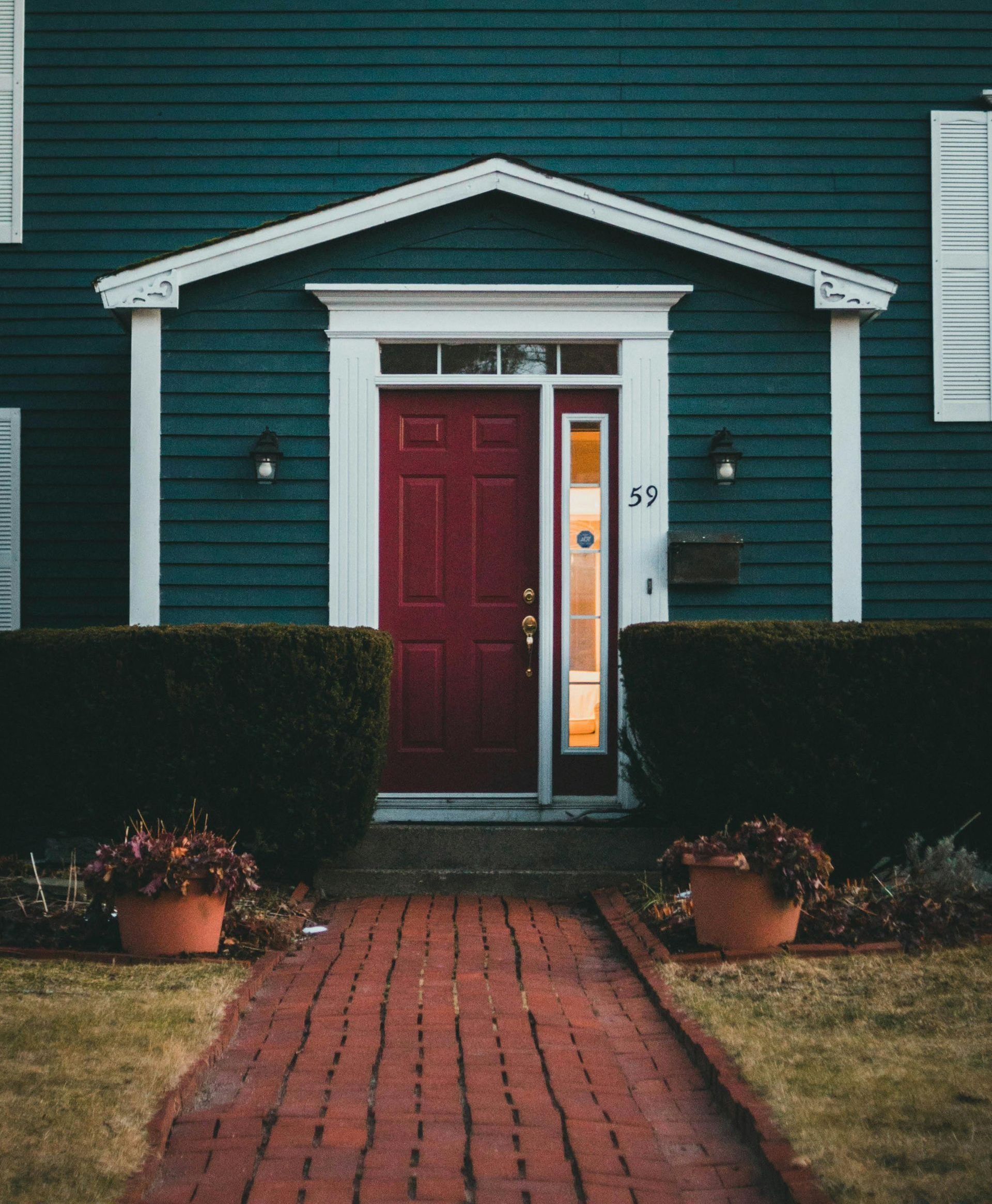 A blue house with a red door and a brick walkway leading to it.