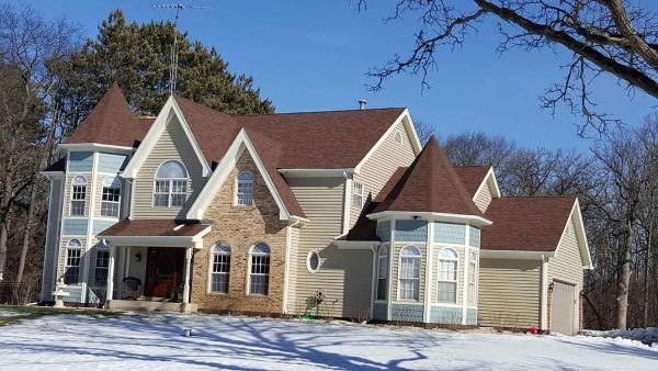 A large house with a red roof is surrounded by snow