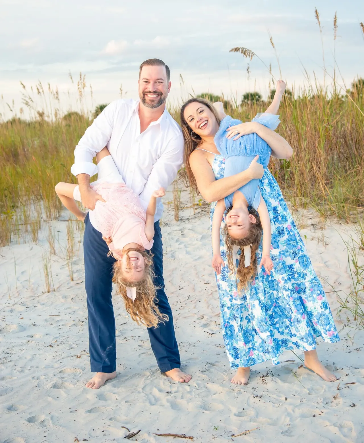 A smiling couple on a sandy beach holding their two children upside down by their legs.