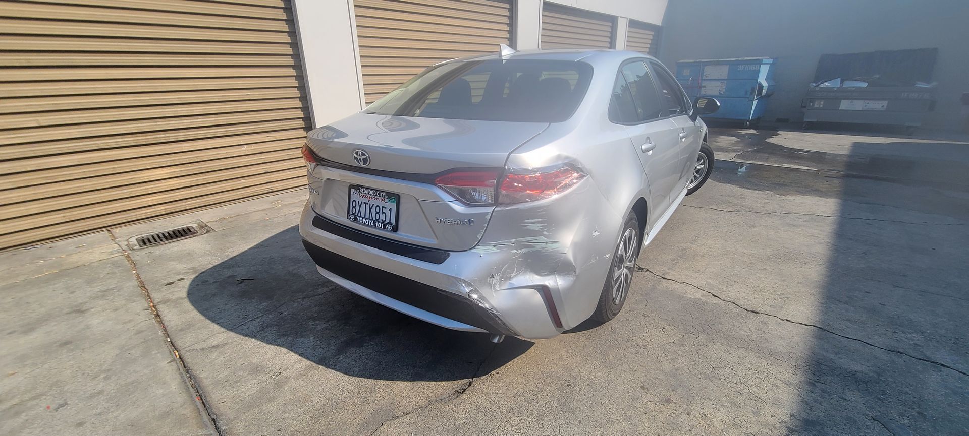 A silver car with a damaged back end is parked in a parking lot.