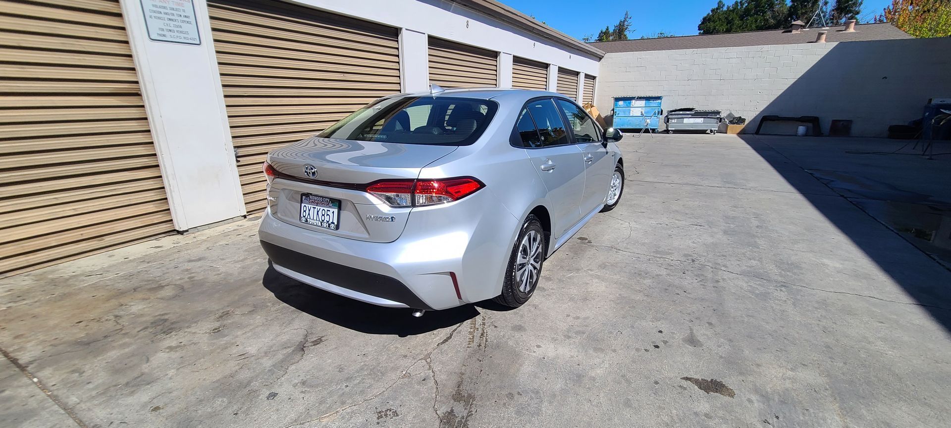 A silver car is parked in a parking lot in front of a garage.