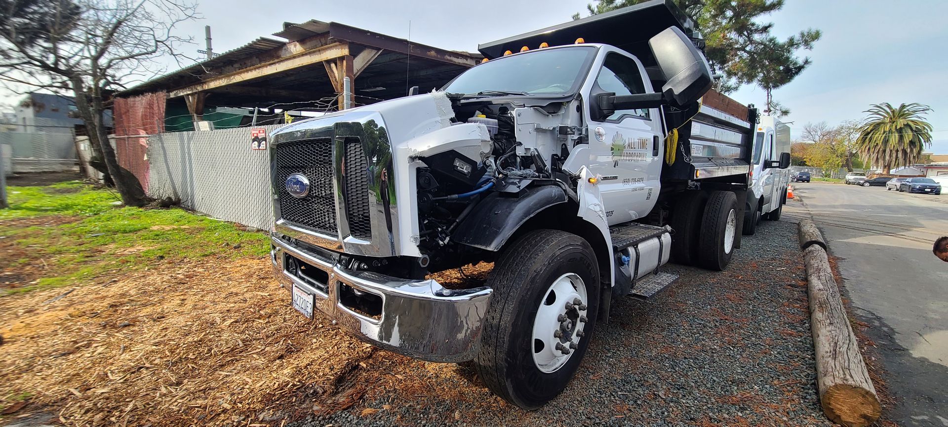 A dump truck is parked on the side of the road next to a log.