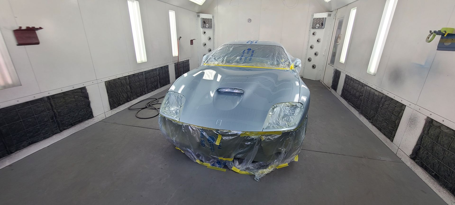 A car is sitting in a paint booth covered in plastic.