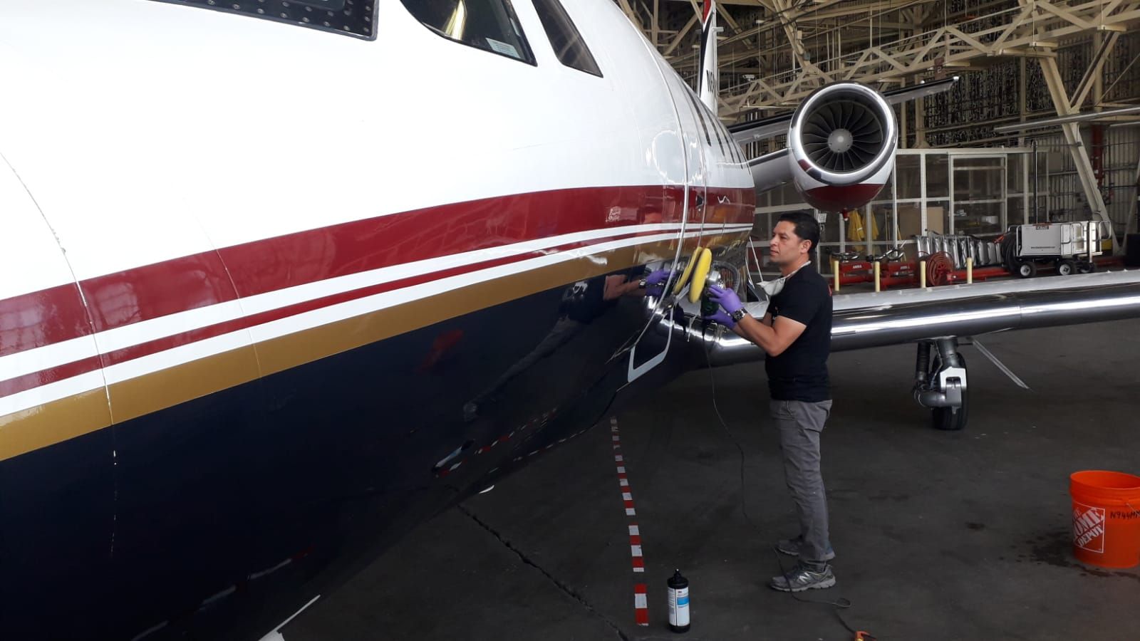 A man is cleaning the side of an airplane in a hangar.