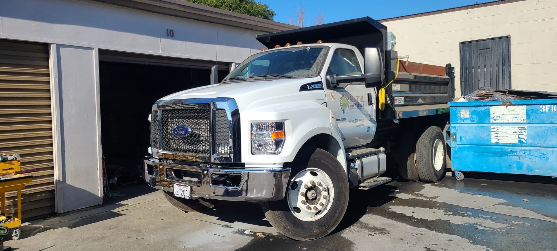 A white dump truck is parked in front of a garage.