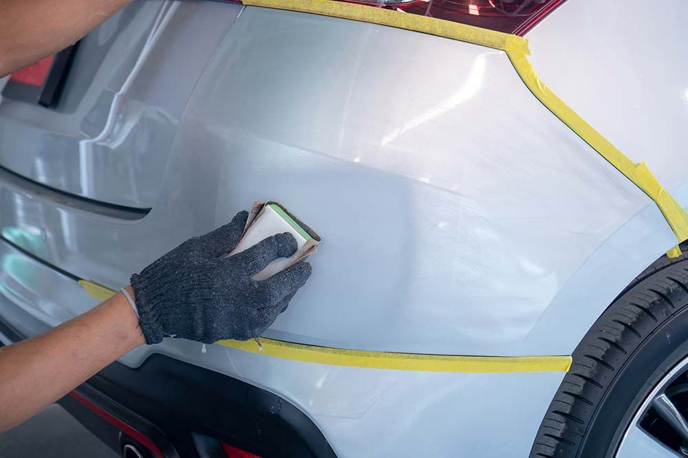 A person is cleaning the bumper of a car with a sponge.