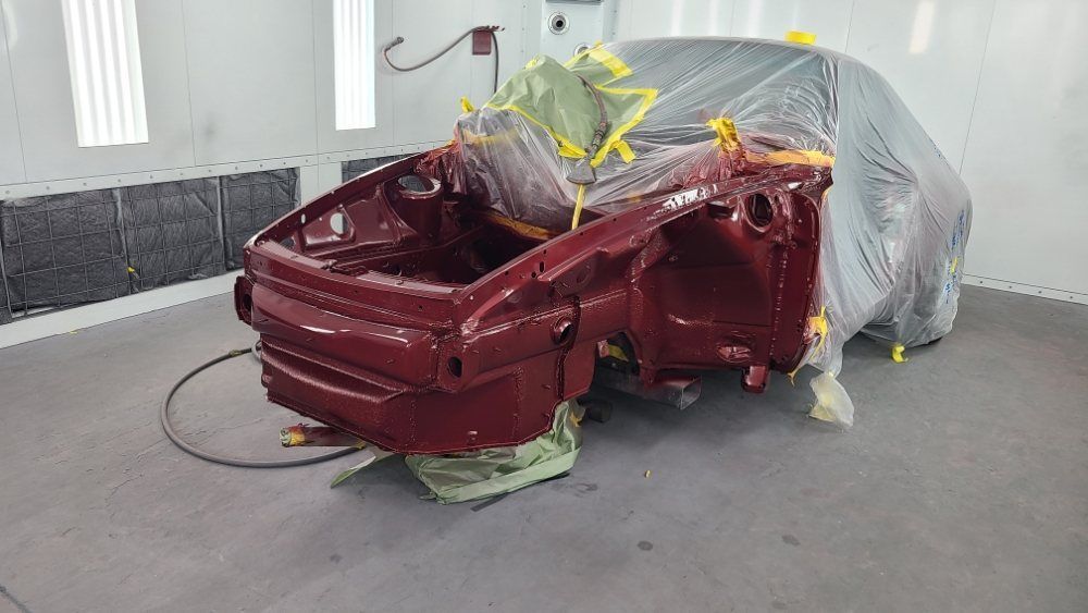 A red car is being painted in a paint booth.