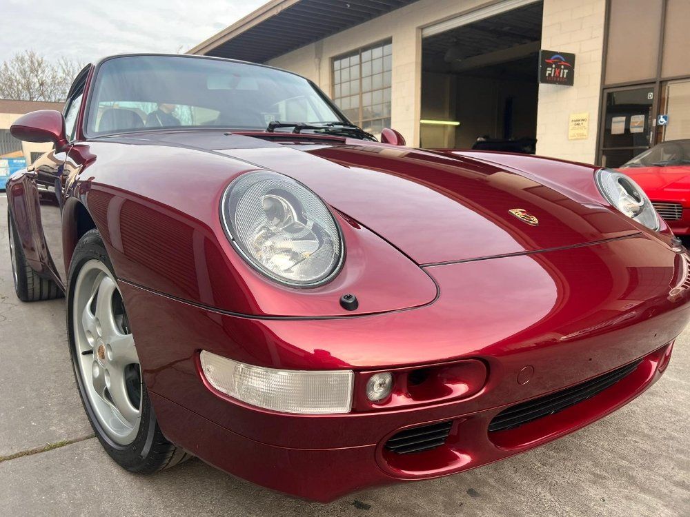 A red porsche 911 is parked in front of a garage.