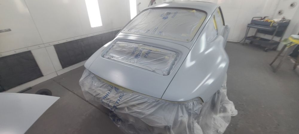 A car is covered in plastic while being painted in a garage.