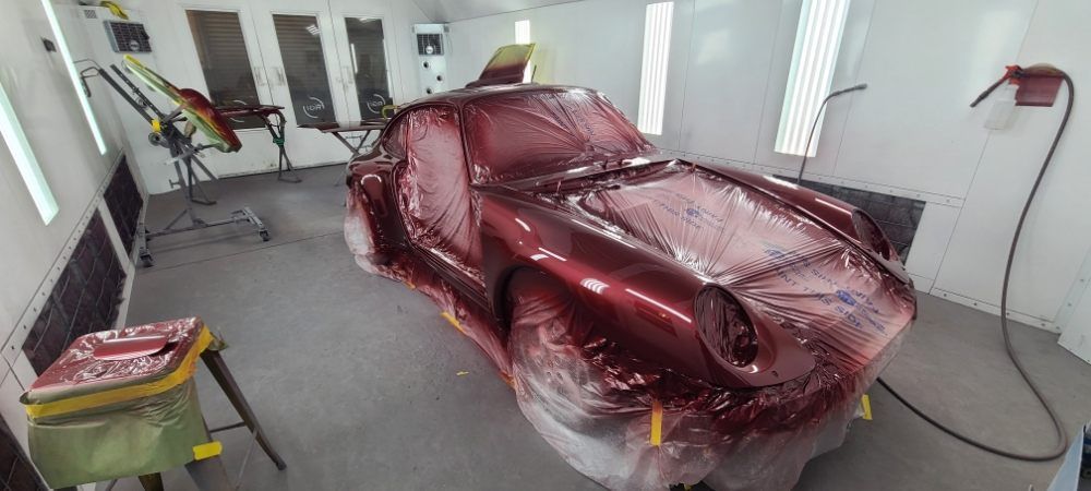 A red car is being painted in a paint booth.