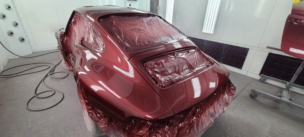 A red car is being painted in a paint booth.