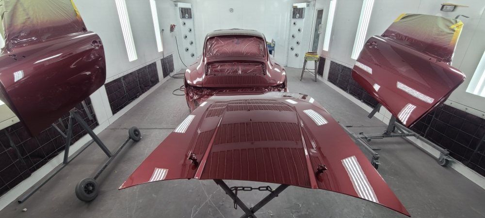 A red car is being painted in a paint booth.