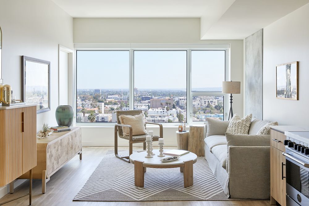 Bright modern living room with large windows, city view, sofa, armchairs, and wooden coffee table