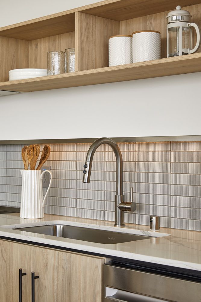 Modern kitchen sink with stainless faucet, wood cabinets, open shelves, and white dishware