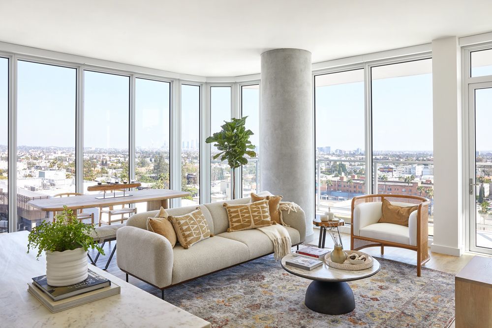 Bright modern living room with floor-to-ceiling windows, beige sofa, armchair, and city skyline views