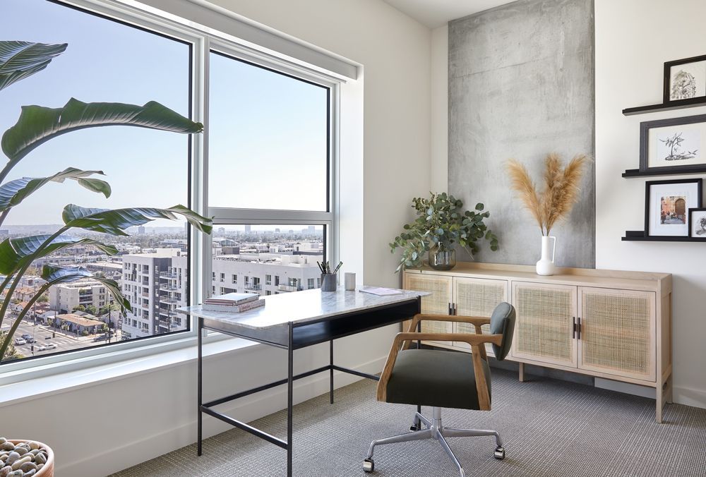 Bright home office with desk, chair, large window, indoor plants, and framed wall art