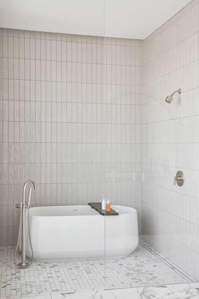 Minimal white-tiled bathroom with a white freestanding tub and handheld shower.