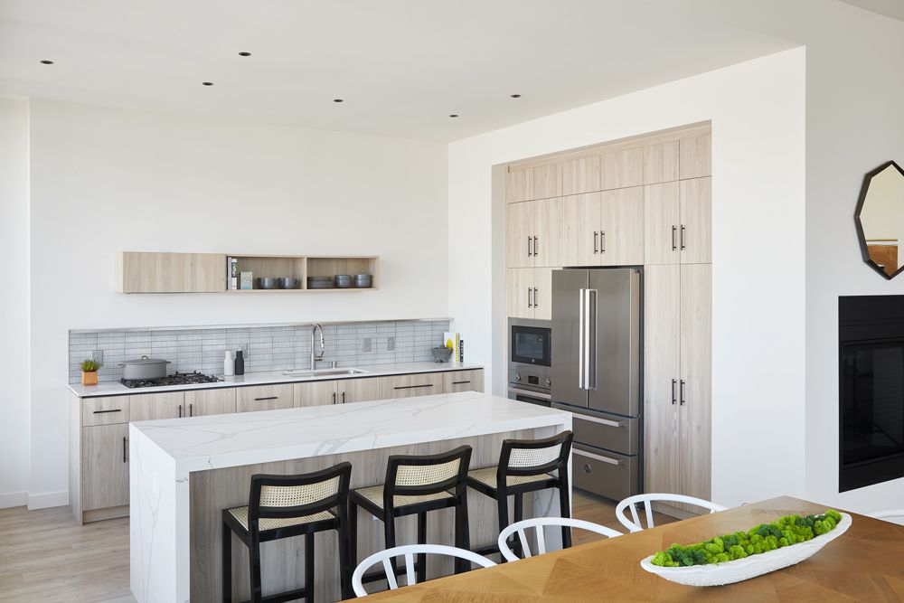 Modern white kitchen with island, stainless steel fridge, beige cabinets, and dining table in foreground