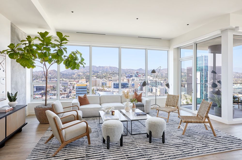 Bright modern living room with large windows, city view, striped rug, and light wood furniture