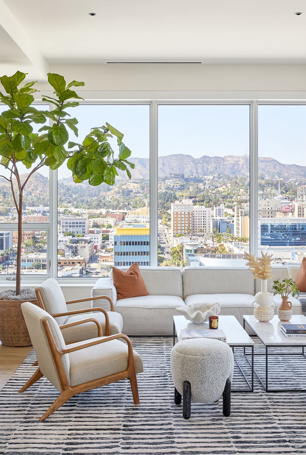 Bright modern living room with white sofa, woven chairs, and city view through large windows