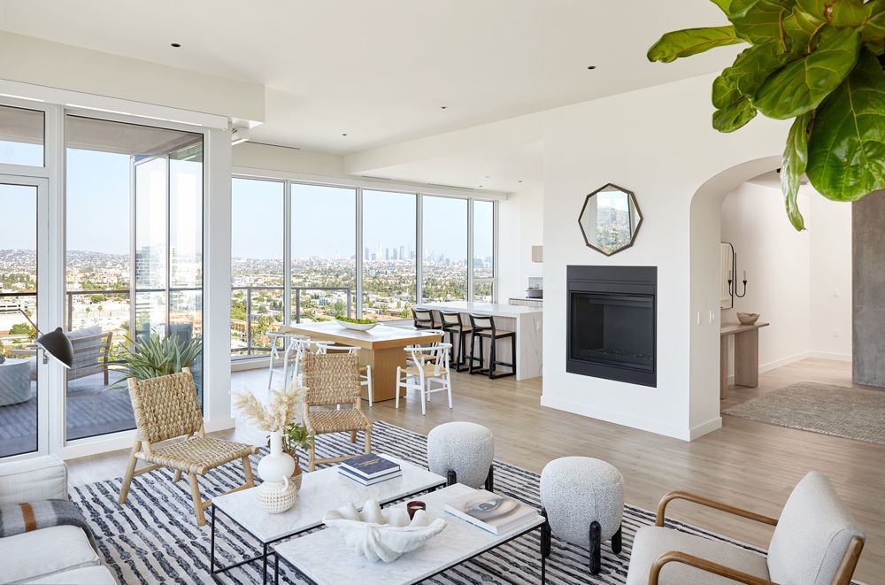 Bright modern living room with city view, white furniture, and dining area by large windows