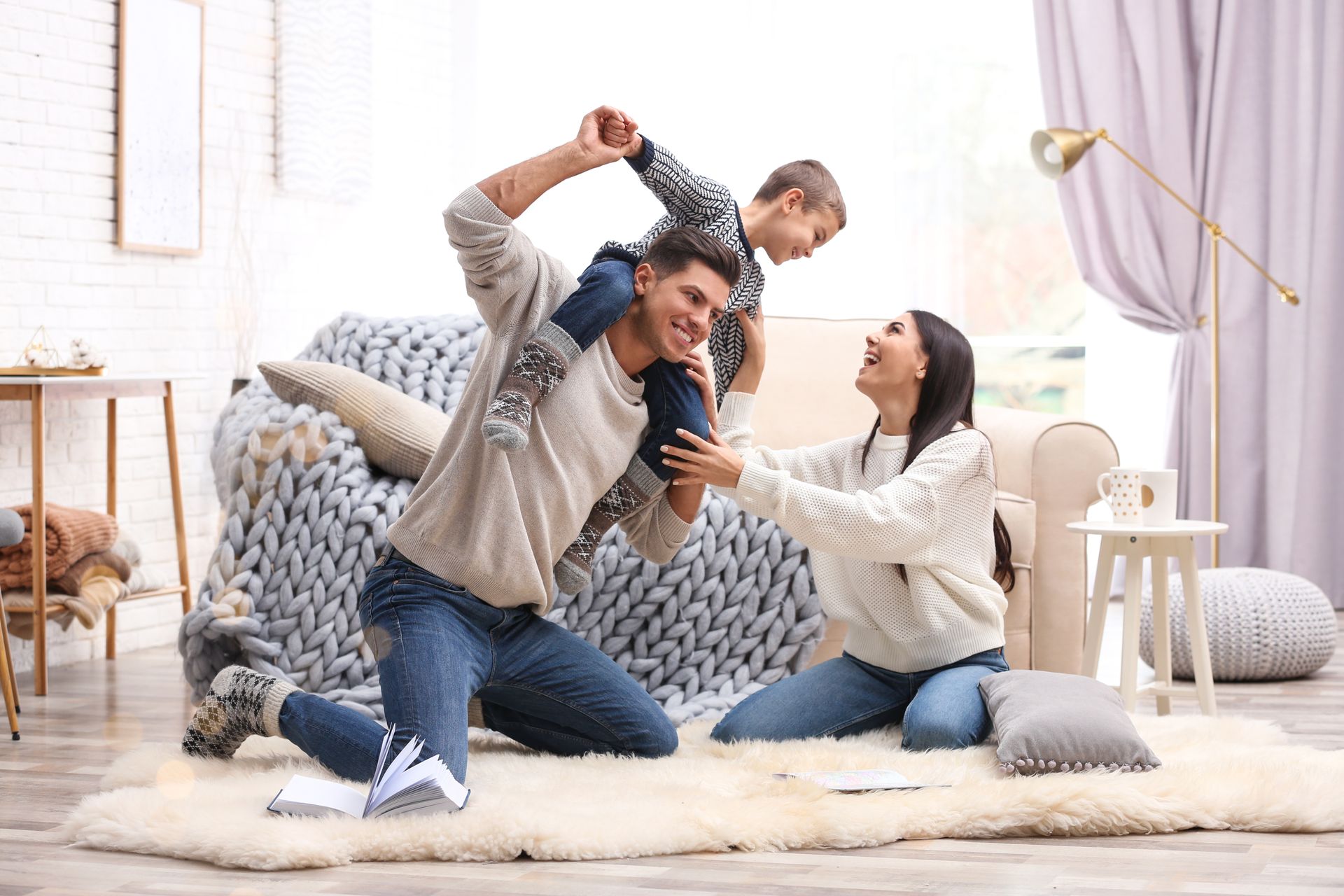 Family playing together on a living room rug, laughing with pillows and a child on shoulders