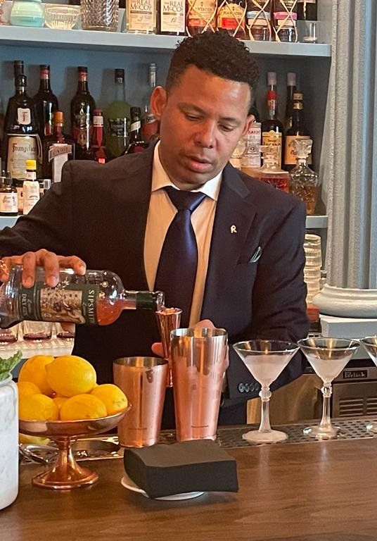 A man in a suit and tie is pouring a drink into a shaker.