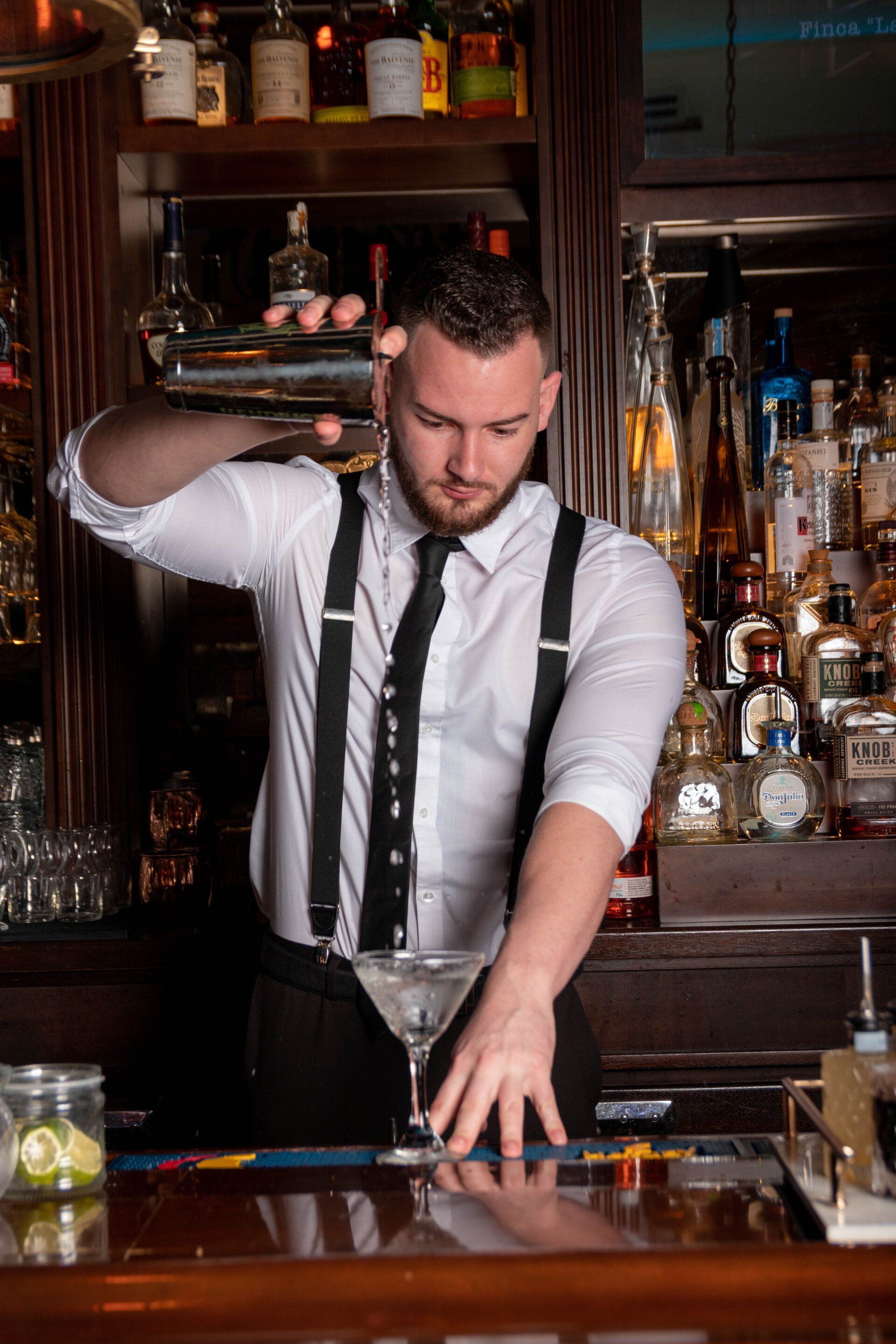 A bartender is making a martini at a bar.