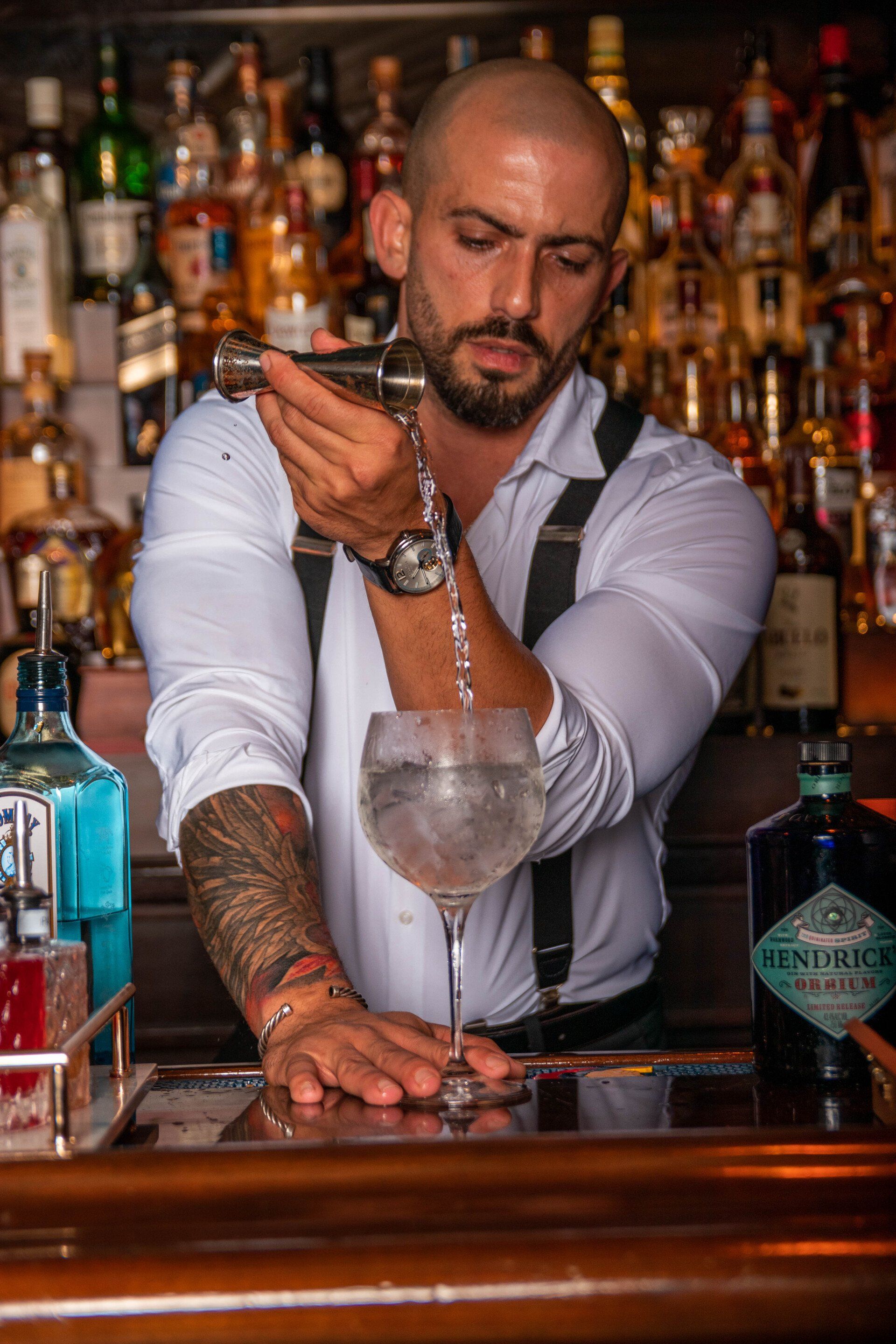 A bartender is pouring a drink into a glass at a bar.