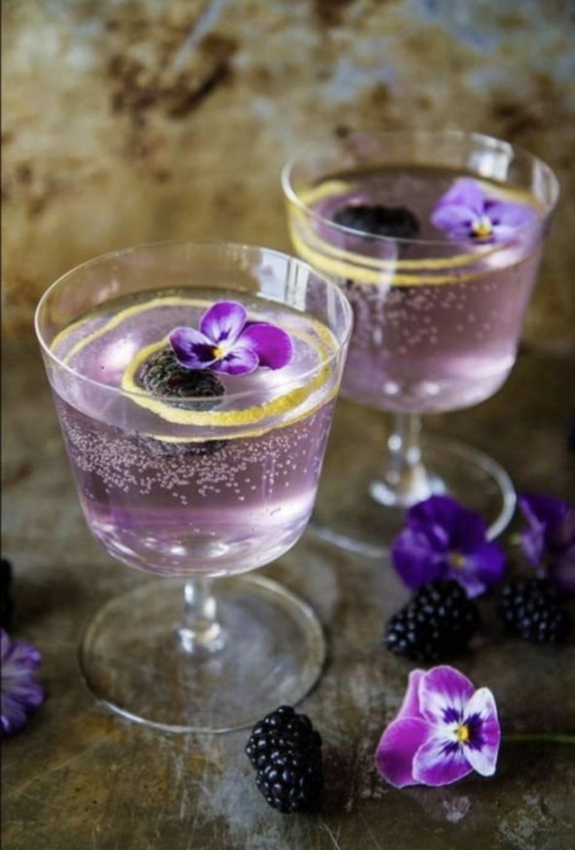 Two wine glasses filled with purple liquid and purple flowers.