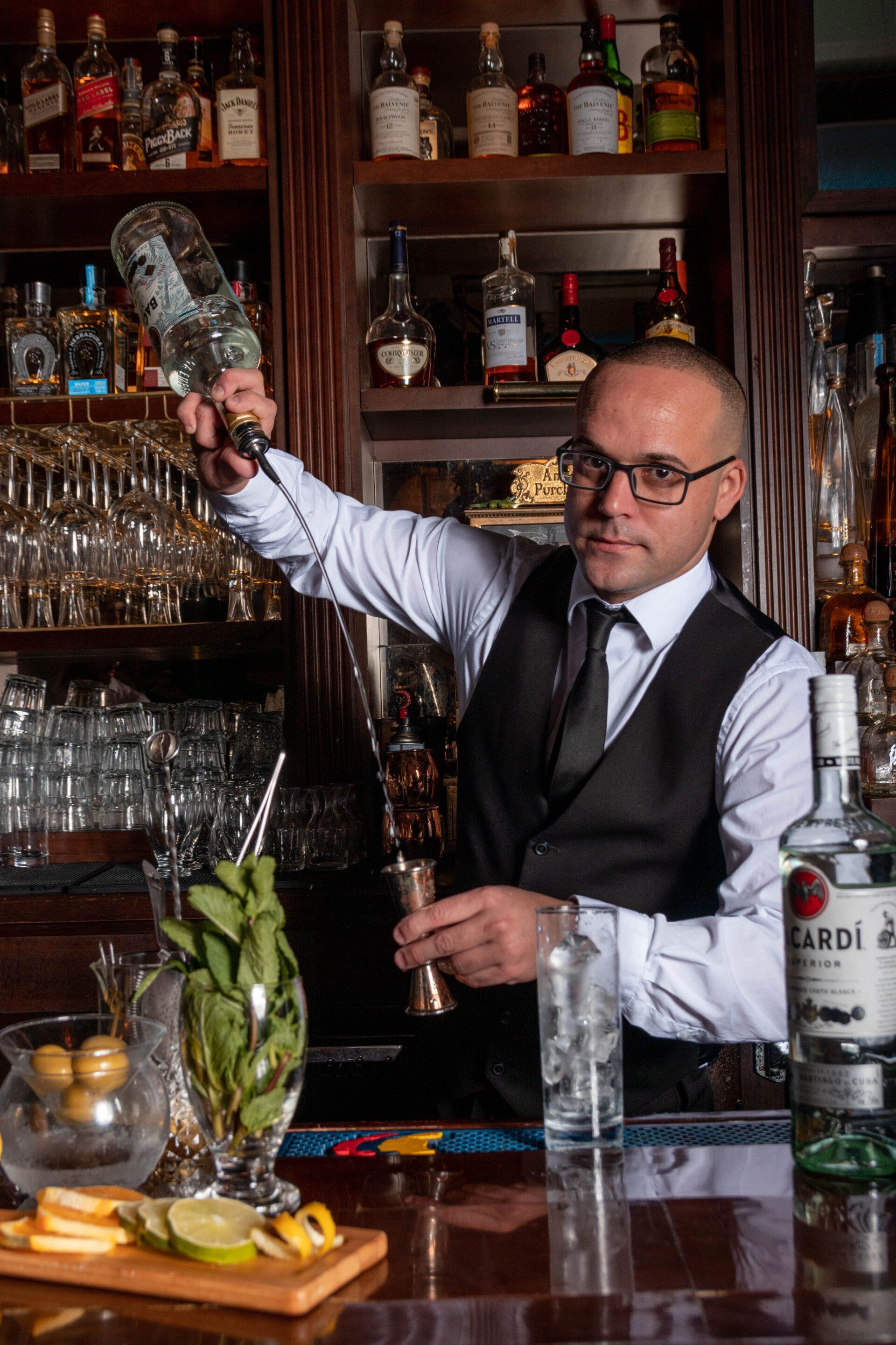 A bartender is pouring a drink into a glass at a bar.
