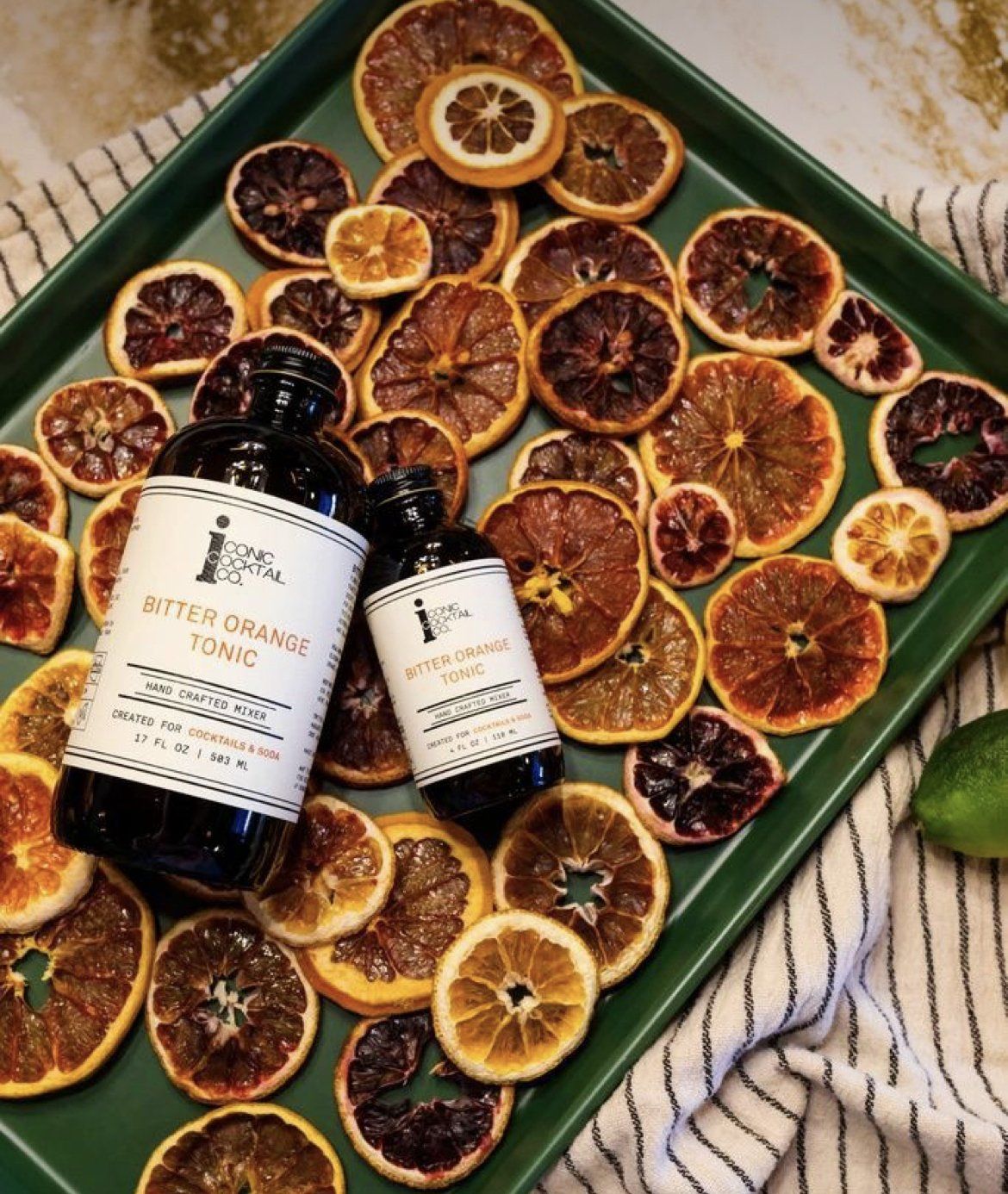 A green tray filled with dried oranges and two bottles of citrus tonic