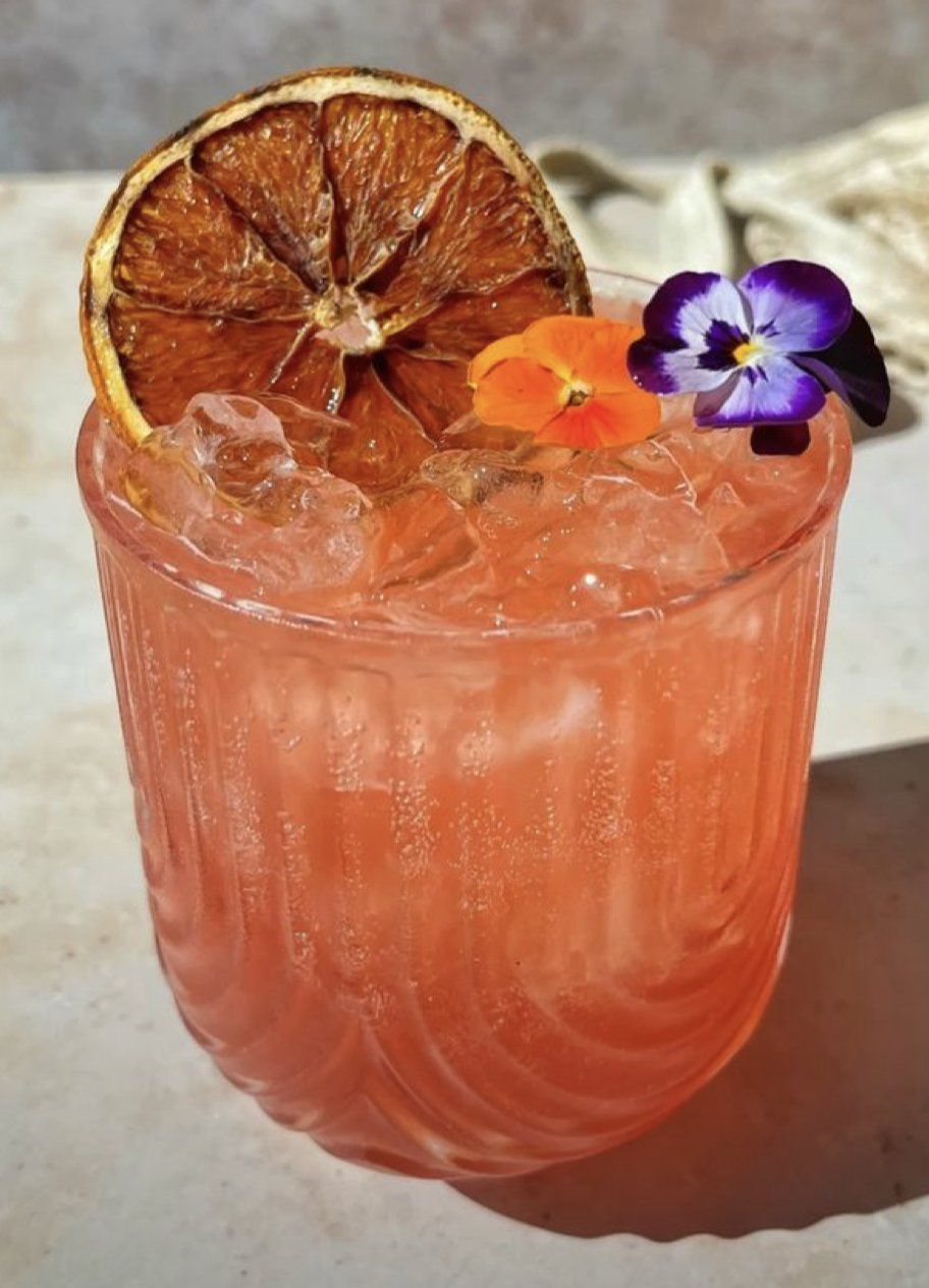 A close up of a drink in a glass with ice and flowers on top.