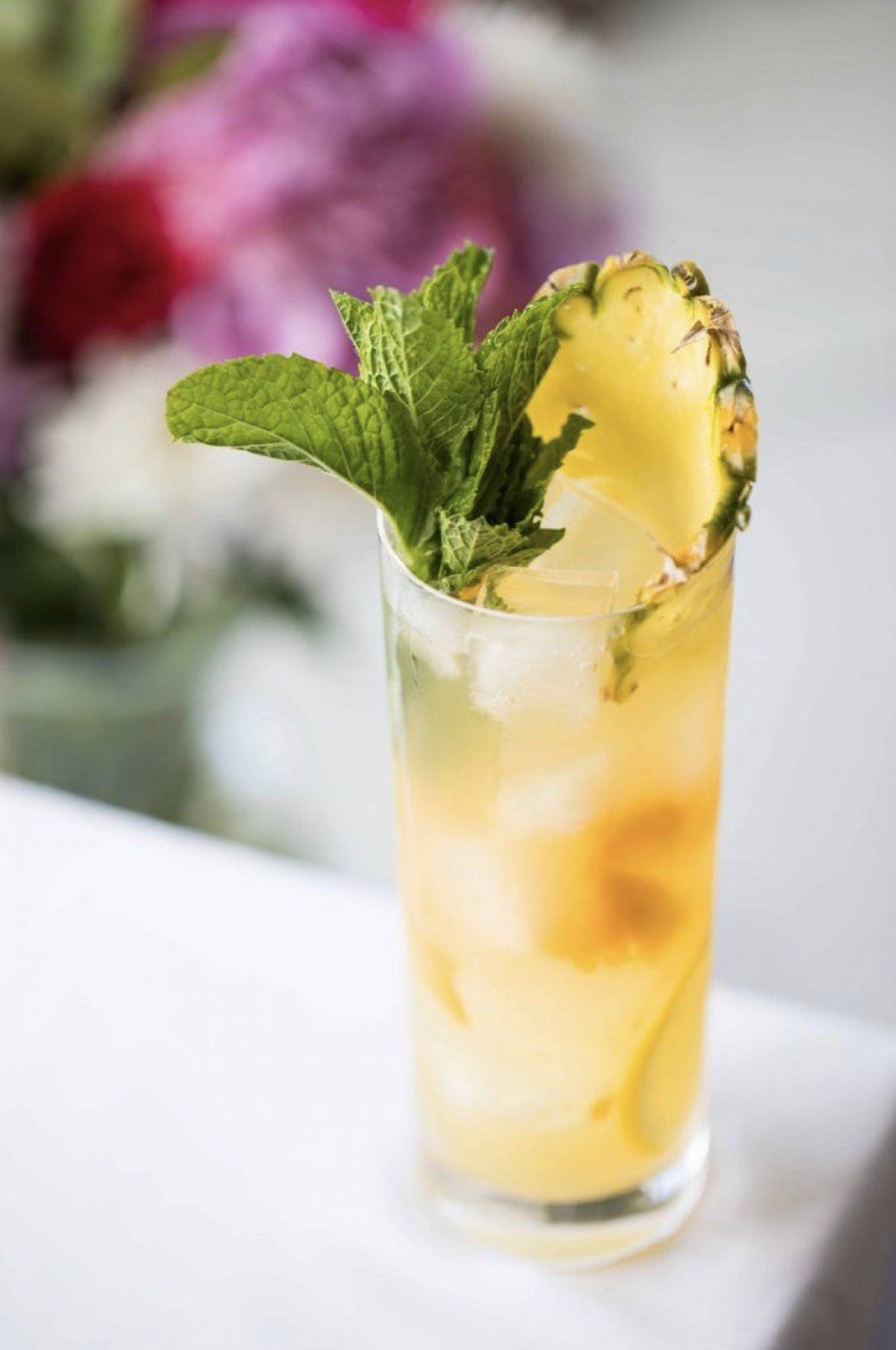 A close up of a pineapple and mint drink in a glass on a table.