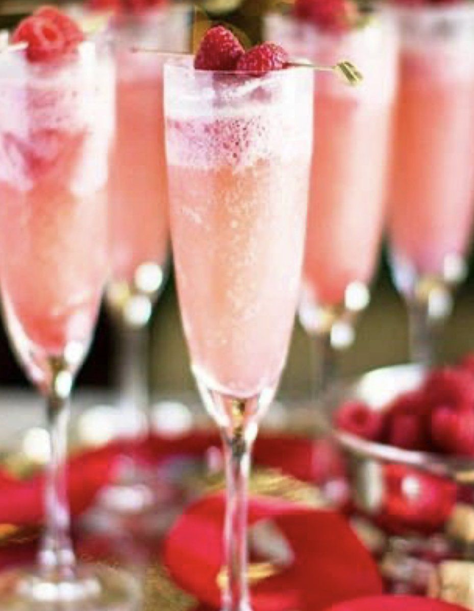 A row of champagne glasses filled with pink liquid and raspberries on top.