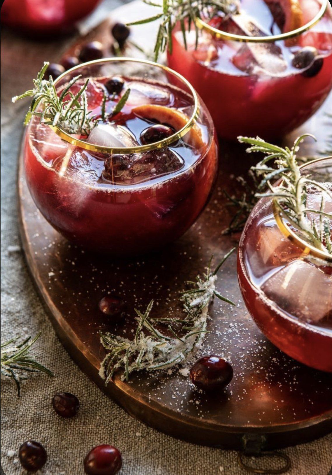 Three glasses of red liquid are sitting on a wooden cutting board.
