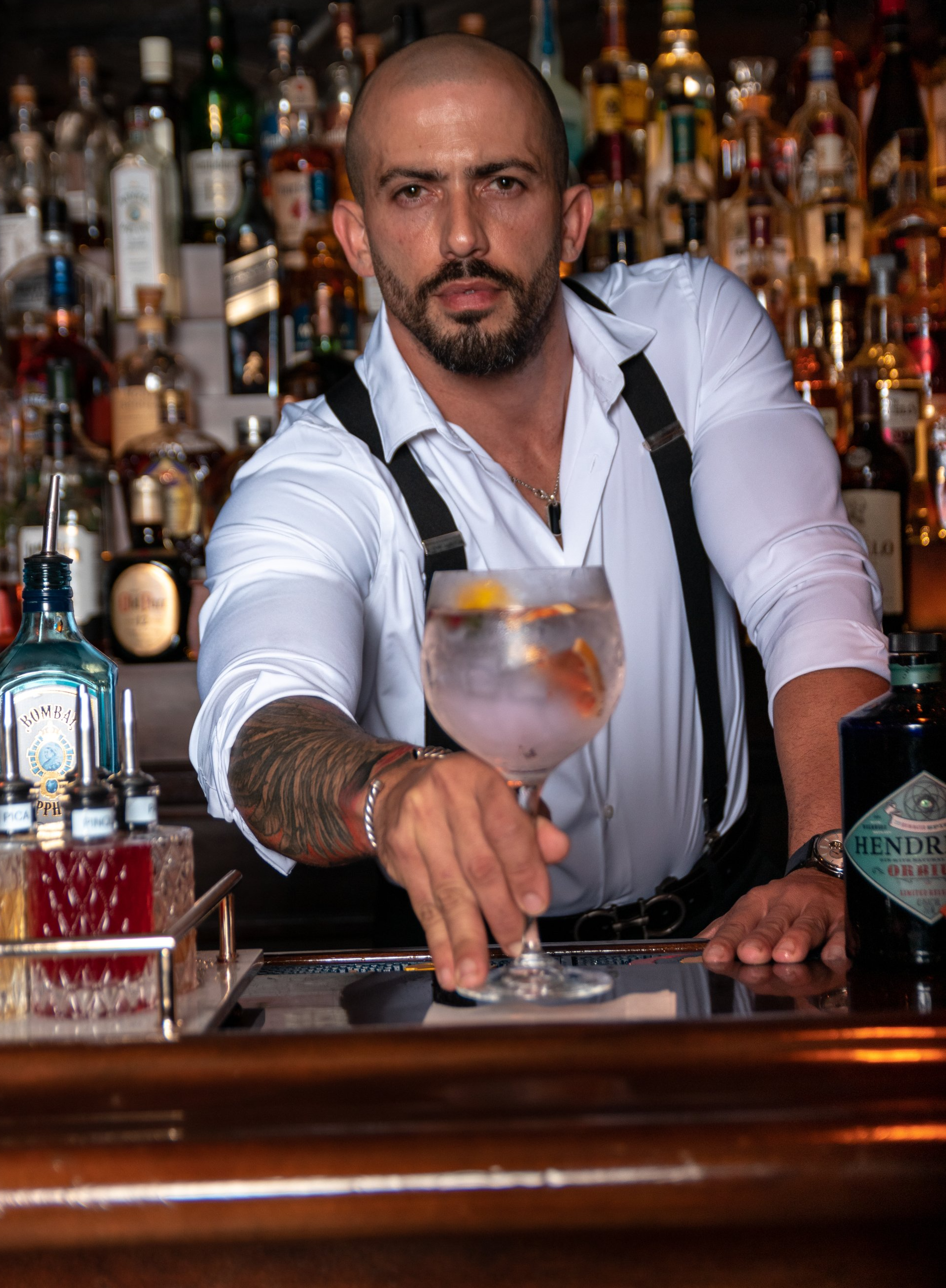 A man is standing behind a bar holding a glass of gin.